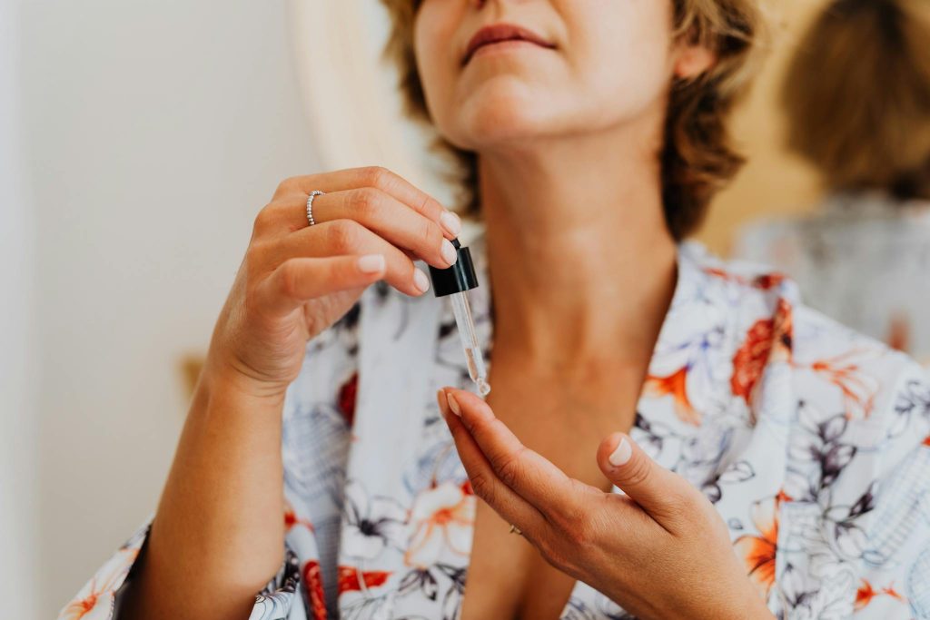 Close-up of a woman in a floral robe applying facial serum using a dropper.