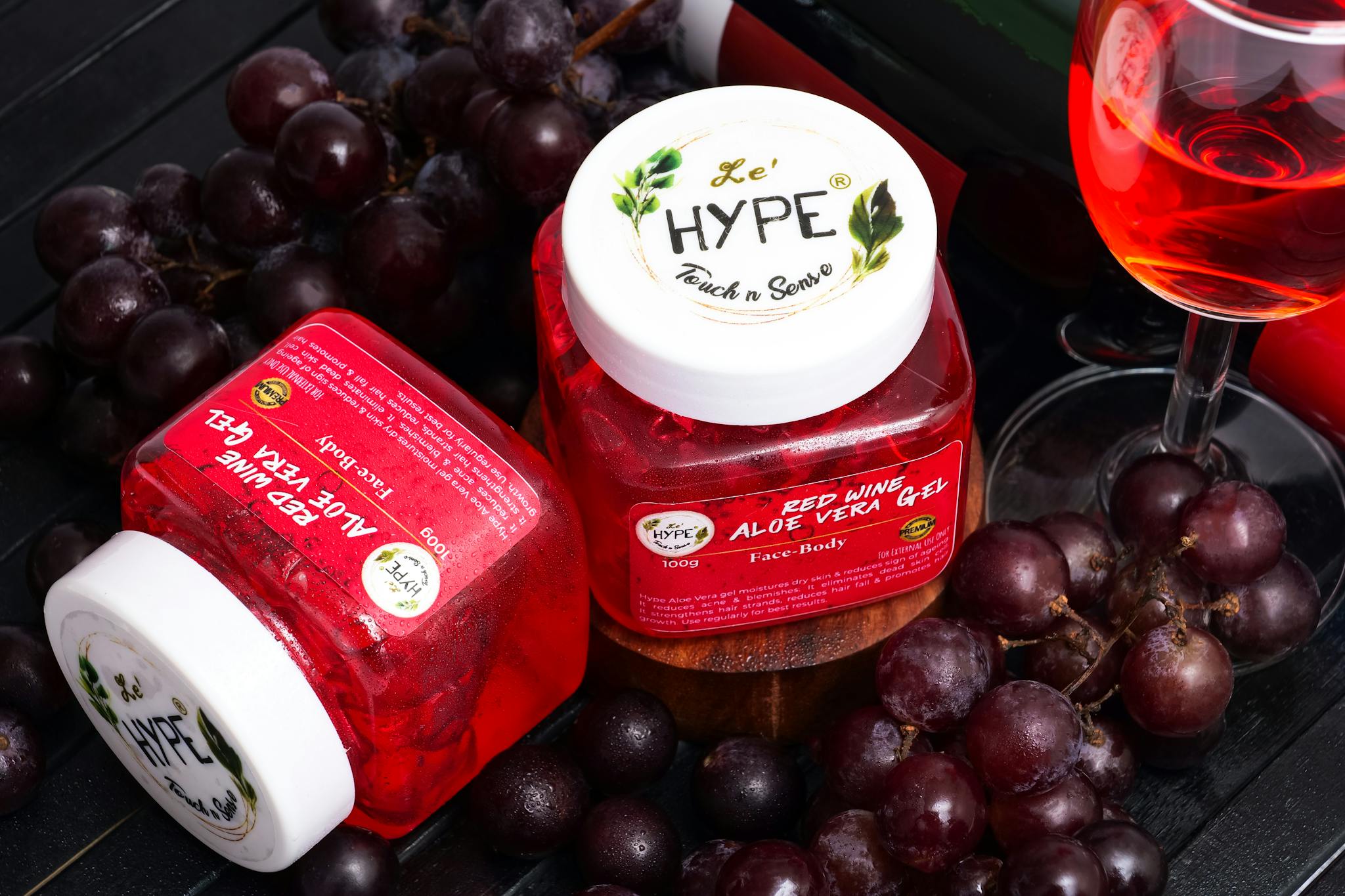 Red wine aloe vera gel jars surrounded by ripe grapes and a glass of wine.